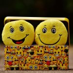 Two yellow smiley plush toys in an emoji-themed box, expressing fun and happiness.