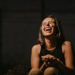 A joyful young woman laughing with confetti on a dark background.