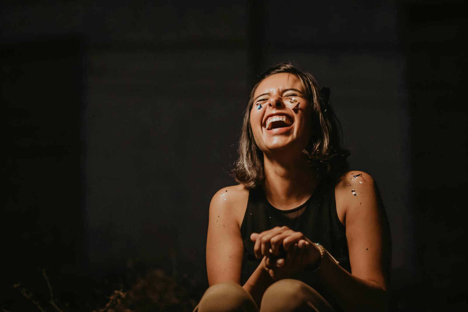 A joyful young woman laughing with confetti on a dark background.