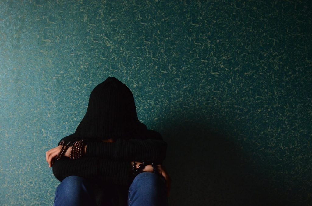 A person sits alone in a hoodie, conveying a sense of solitude and introspection.